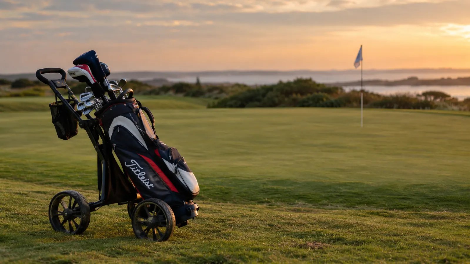 A golf bag on a push cart parked beside the 18th green in soft evening light