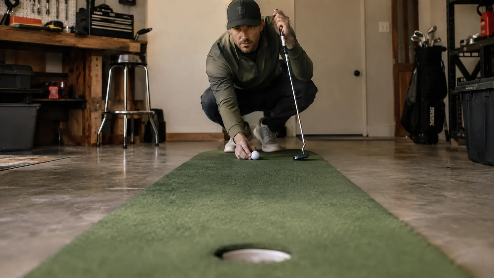 A golfer kneeling behind a golf ball on a practice putting surface, checking the line toward the cup